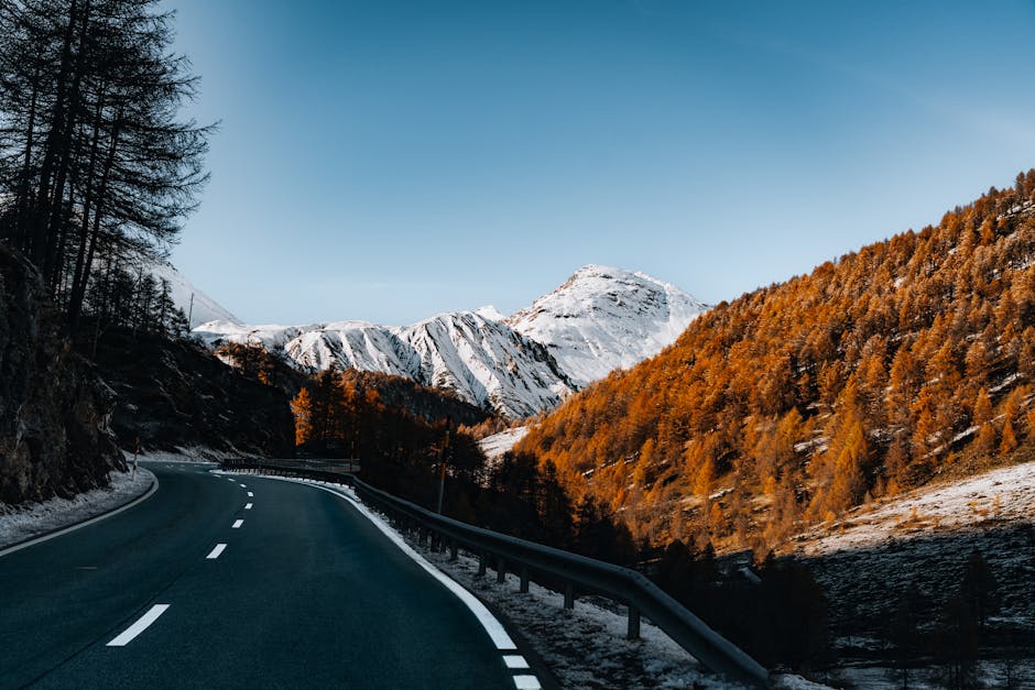 Curving road through a picturesque alpine landscape with snow-capped peaks.
