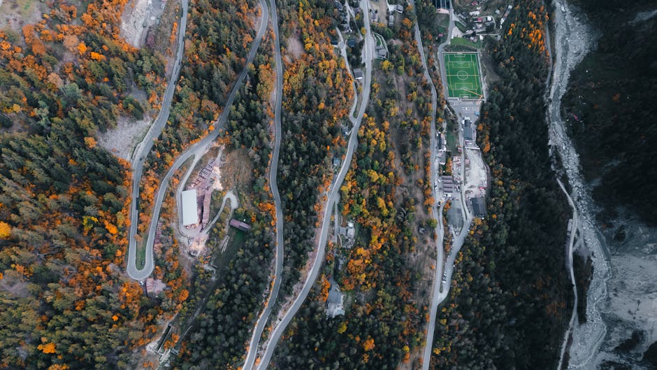 Stunning aerial view of winding mountain roads surrounded by autumn foliage and a football field in Anniviers, Switzerland.